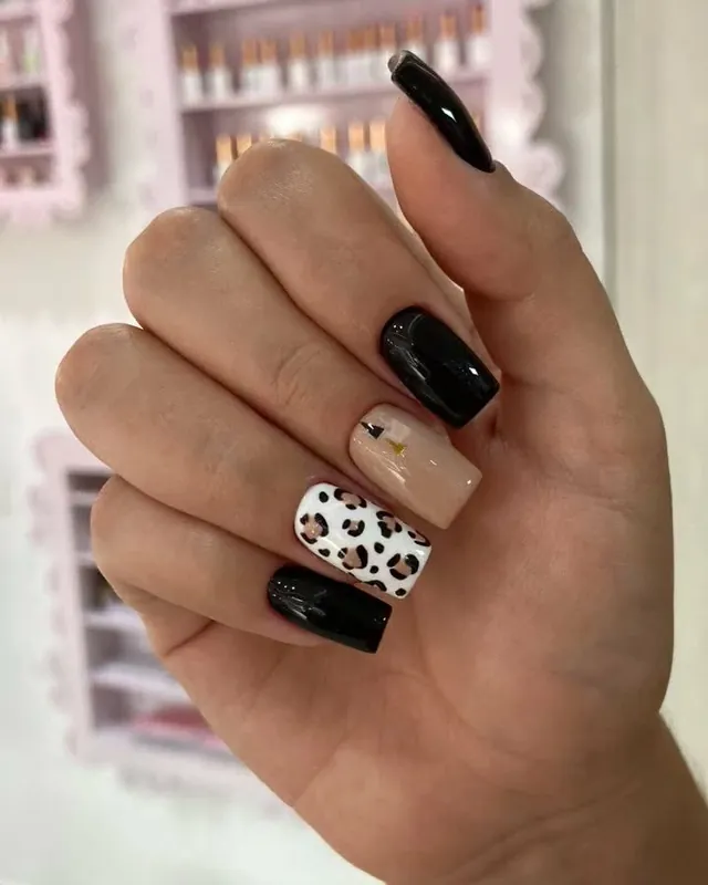 Uñas negras brillantes con una uña de animal print de leopardo sobre base blanca.