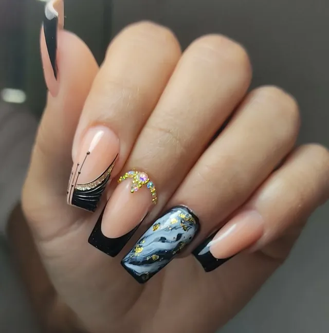 Uñas negras con una uña de efecto mármol gris, hoja dorada y pedrería cristalina.