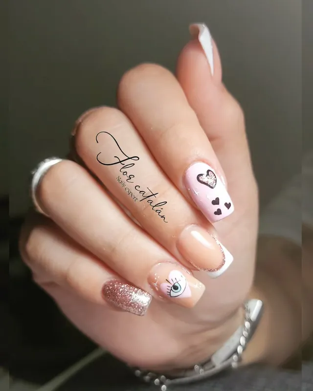 Uñas en rosa claro decoradas con corazones, un ojo turco y glitter oro rosa.
