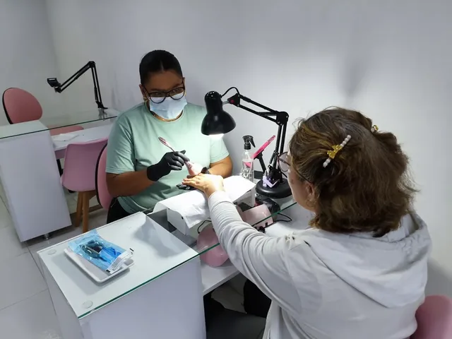 Manicurista con tapabocas y guantes atendiendo a una clienta en la mesa de manicura, con el instrumental esterilizado empacado sobre la bandeja.