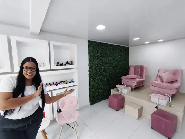 Flor Catalán, sonriendo, muestra el interior del estudio: la pared de esmaltes, el muro verde y los dos sillones rosados de pedicura.